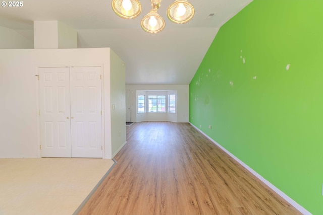 interior space featuring baseboards, light wood-style flooring, lofted ceiling, and a notable chandelier