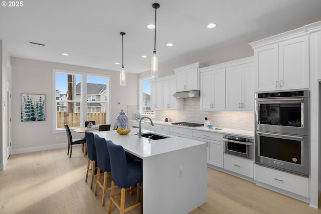 17716 NW Layla Dr Lot 28, Portland, OR 97229 - kitchen with stainless steel appliances, a sink, decorative backsplash, a kitchen island with sink, and light wood-type flooring