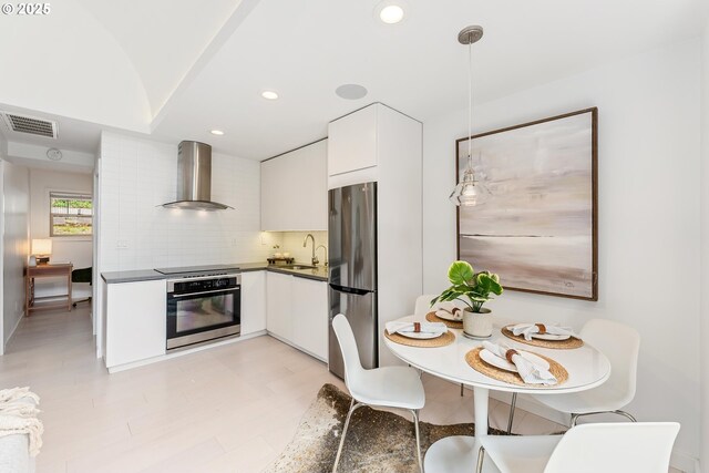 859 SW Broadway Dr Unit 41, Portland, OR 97201 - kitchen featuring dark countertops, wall chimney exhaust hood, white cabinets, a sink, and appliances with stainless steel finishes