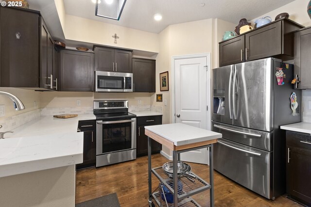 kitchen featuring appliances with stainless steel finishes, dark wood-style flooring, dark brown cabinetry, and light stone countertops