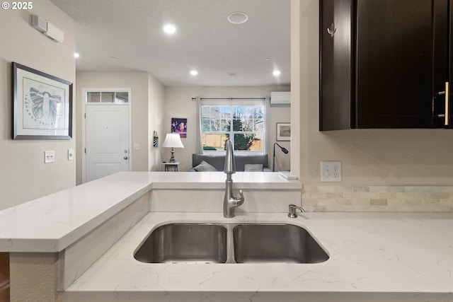 kitchen featuring recessed lighting, a wall mounted air conditioner, a sink, and light stone countertops