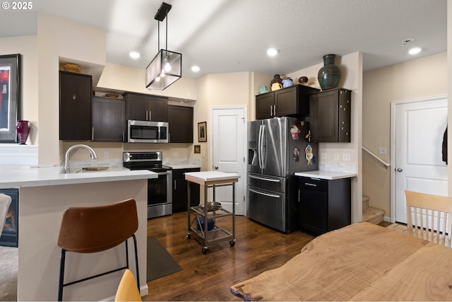 kitchen with appliances with stainless steel finishes, dark wood-style flooring, a peninsula, light countertops, and a sink