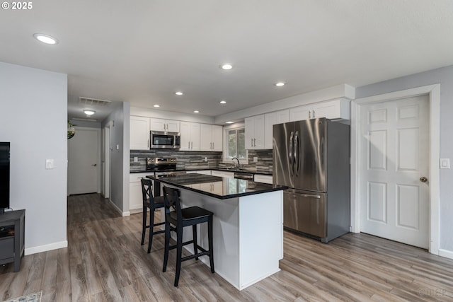 kitchen with a sink, appliances with stainless steel finishes, wood finished floors, and white cabinets