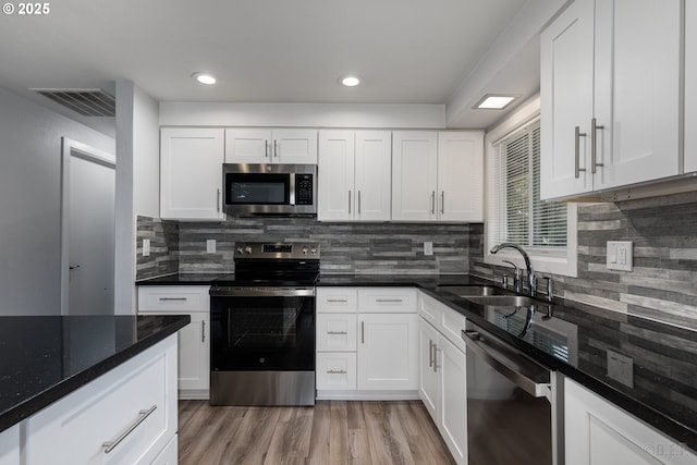 kitchen with white cabinets, appliances with stainless steel finishes, a sink, light wood-type flooring, and backsplash