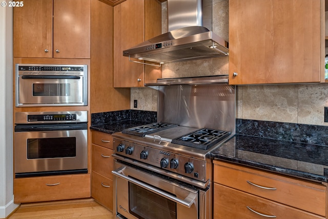 16215 SE Rivershore Dr, Vancouver, WA 98683 - kitchen with wall chimney exhaust hood, appliances with stainless steel finishes, dark stone counters, and brown cabinetry