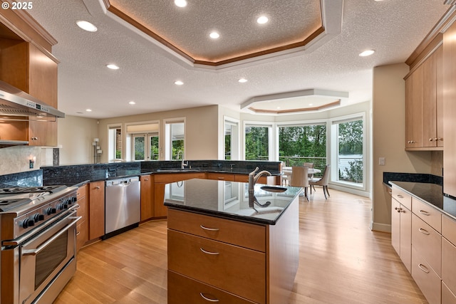 16215 SE Rivershore Dr, Vancouver, WA 98683 - kitchen featuring appliances with stainless steel finishes, a textured ceiling, light wood-type flooring, a kitchen island with sink, and dark stone countertops