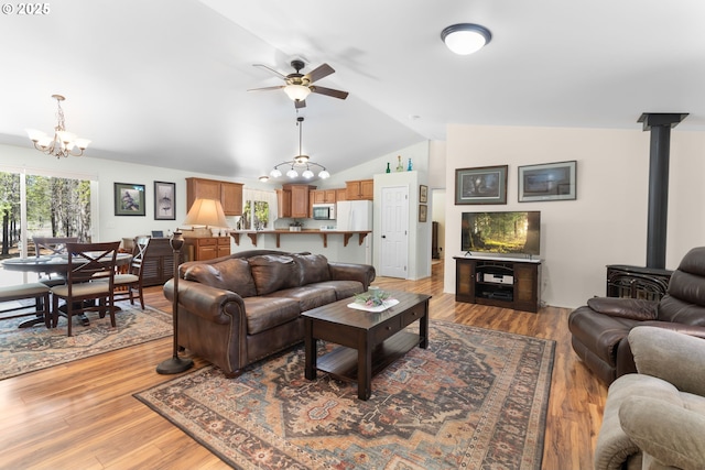 living area featuring a chandelier, a ceiling fan, vaulted ceiling, light wood finished floors, and a wood stove