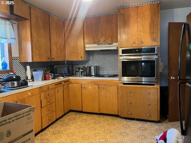 13727 SE Raymond St, Portland, OR 97236 - kitchen with stainless steel oven, under cabinet range hood, light countertops, black microwave, and decorative backsplash