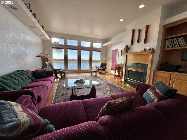 living area featuring built in features, a tile fireplace, light wood-style flooring, a water view, and recessed lighting