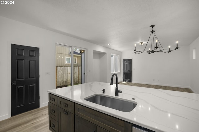 kitchen featuring light stone countertops, a sink, light wood-style floors, decorative light fixtures, and open floor plan