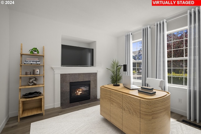 living area with a tiled fireplace, visible vents, baseboards, and wood finished floors