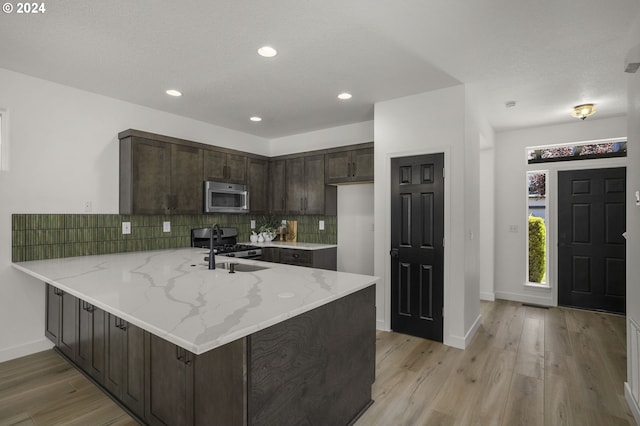 kitchen with a sink, backsplash, appliances with stainless steel finishes, a peninsula, and dark brown cabinets