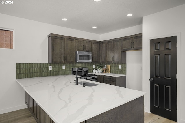 kitchen with light stone counters, tasteful backsplash, stainless steel appliances, dark brown cabinetry, and a peninsula