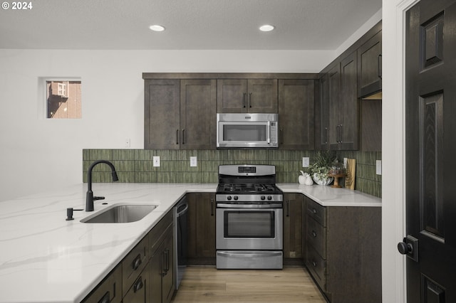 kitchen featuring a sink, tasteful backsplash, stainless steel appliances, dark brown cabinetry, and light stone countertops