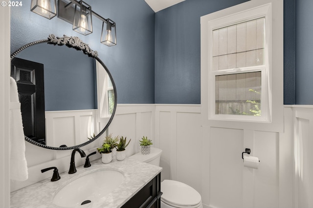 half bath with a wainscoted wall, toilet, and vanity