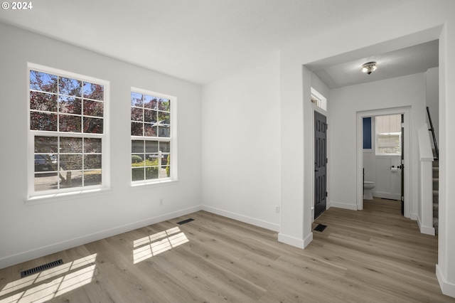 empty room with visible vents, stairs, light wood-type flooring, and baseboards