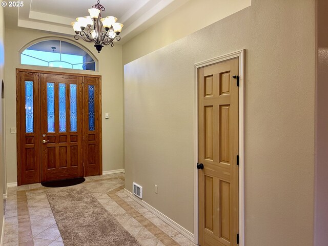 entryway with a raised ceiling, baseboards, visible vents, and a chandelier