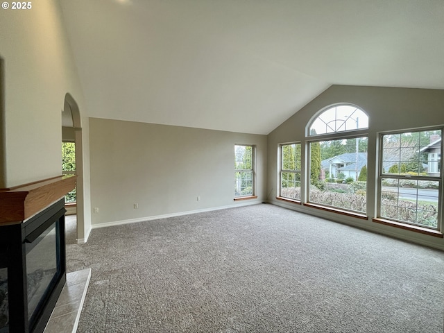 unfurnished living room featuring a glass covered fireplace, carpet, baseboards, and arched walkways