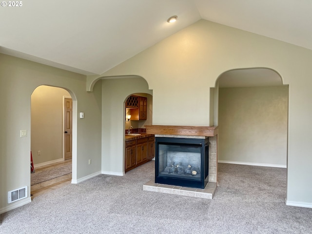 unfurnished living room featuring visible vents, baseboards, light colored carpet, vaulted ceiling, and a sink