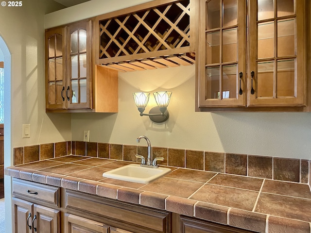 kitchen with a sink, glass insert cabinets, arched walkways, and tile counters