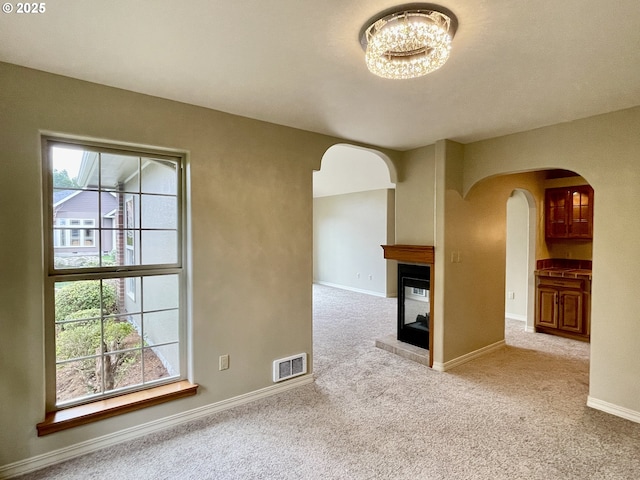 carpeted empty room with visible vents, baseboards, a multi sided fireplace, arched walkways, and a notable chandelier