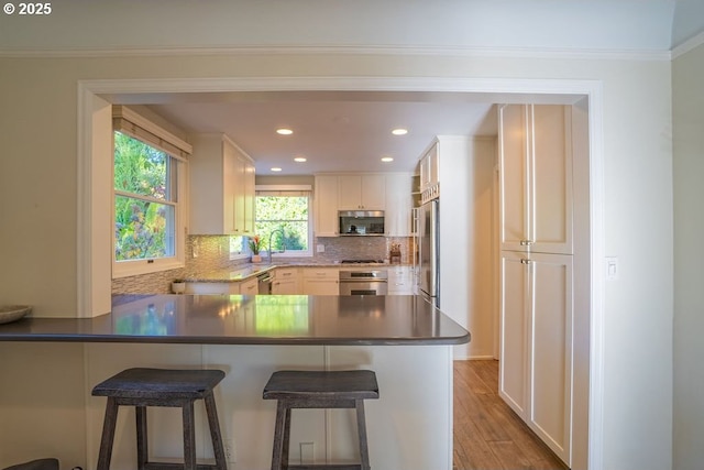 kitchen with kitchen peninsula, hardwood / wood-style flooring, stainless steel appliances, decorative backsplash, and white cabinets