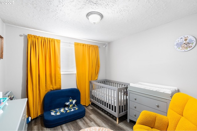 bedroom with dark hardwood / wood-style flooring, a nursery area, and a textured ceiling