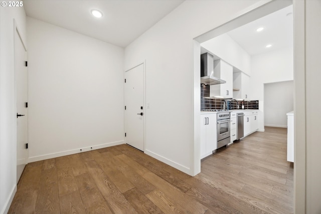 kitchen featuring stainless steel appliances, white cabinetry, light wood finished floors, and wall chimney exhaust hood