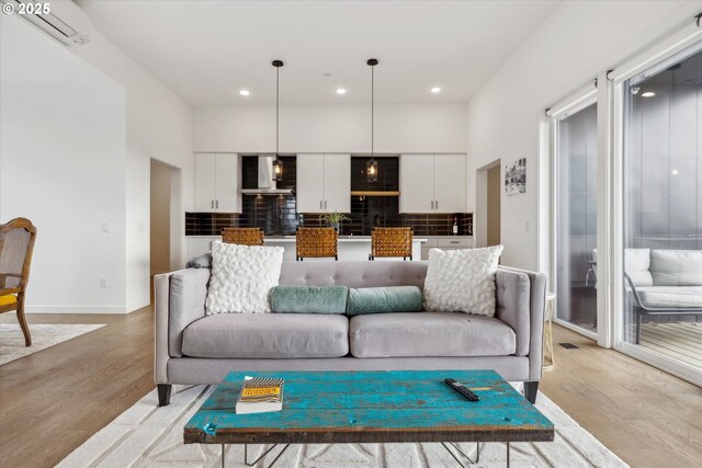 living room with light wood-type flooring, recessed lighting, a wall unit AC, and baseboards