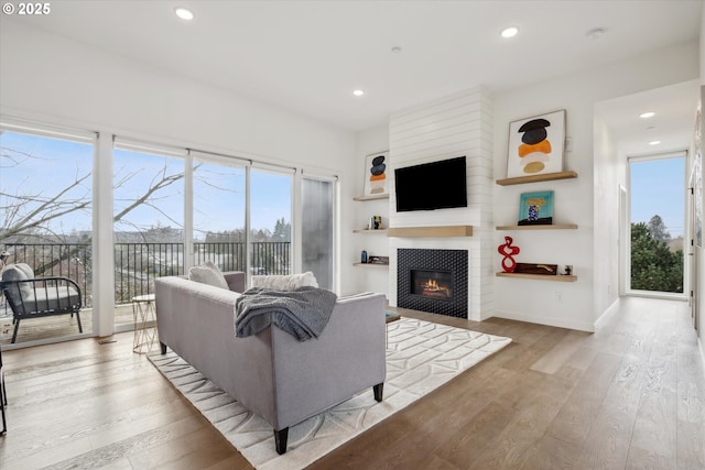 living room featuring a tile fireplace, recessed lighting, baseboards, and wood finished floors