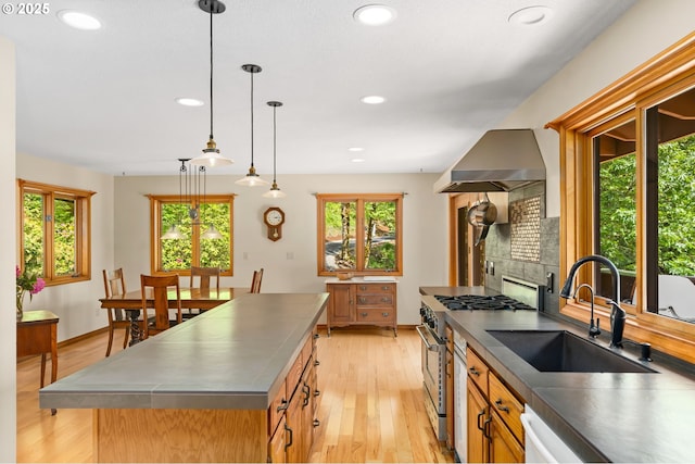 kitchen featuring stainless steel countertops, high end stainless steel range oven, a sink, wall chimney range hood, and light wood-type flooring