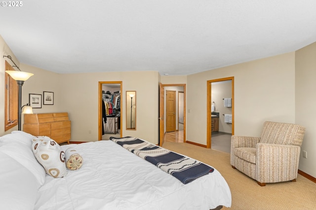 bedroom featuring light colored carpet, a walk in closet, ensuite bathroom, baseboards, and a closet