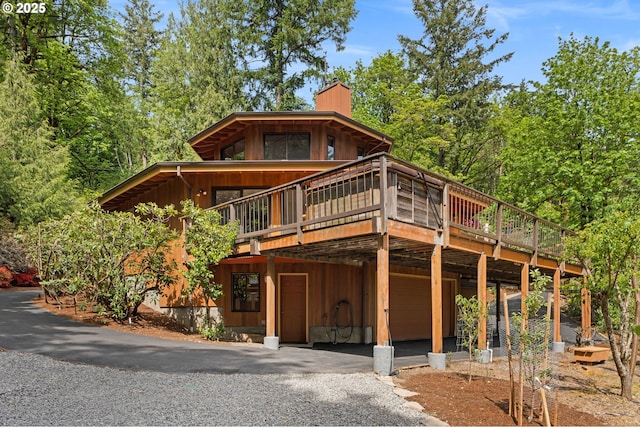 view of front of property with a garage, a chimney, a deck, and asphalt driveway