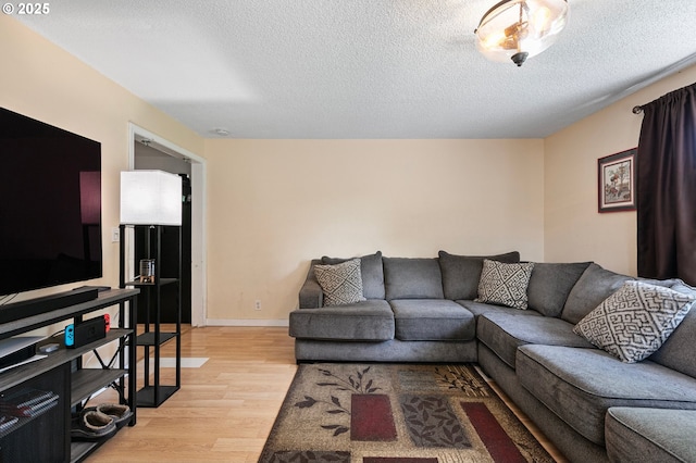 living area featuring a textured ceiling, light wood-style floors, and baseboards