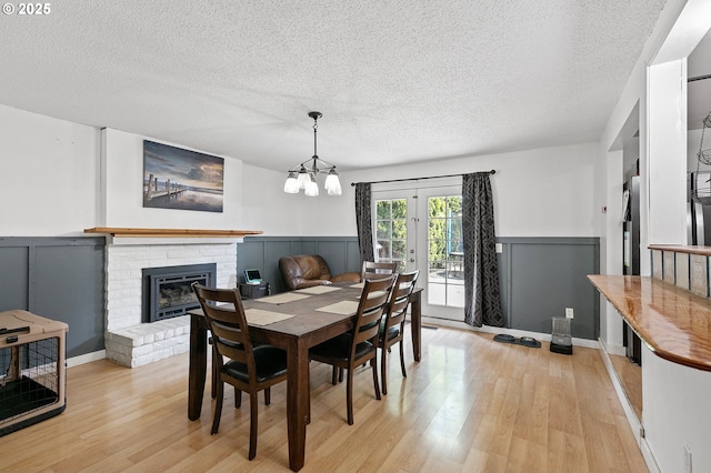dining area with a brick fireplace, a textured ceiling, and light wood-style floors