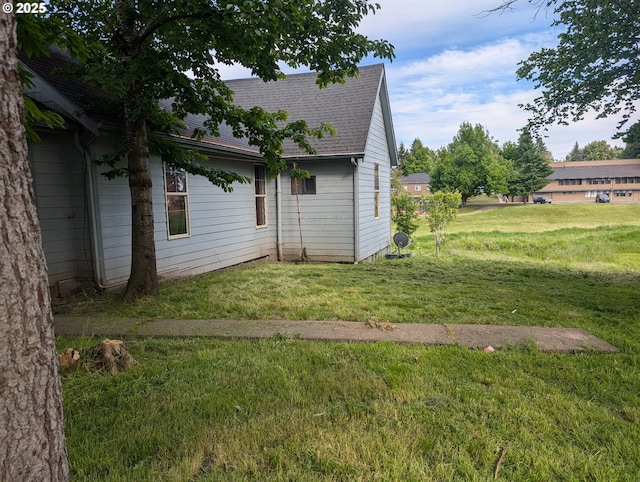 view of side of property with roof with shingles and a yard