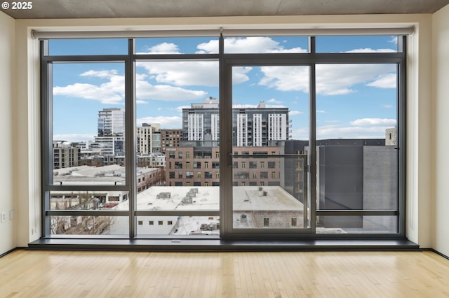 unfurnished room with a view of city, wood finished floors, baseboards, and expansive windows