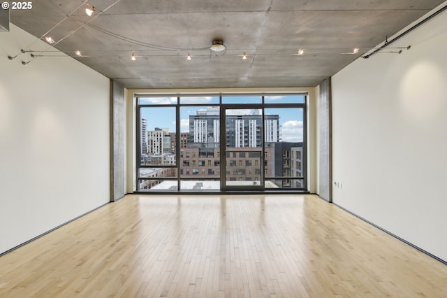 empty room featuring a city view, a wall of windows, and wood finished floors