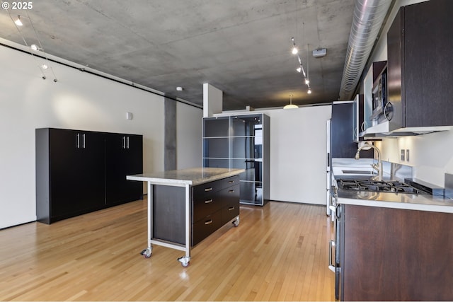 kitchen with light wood-type flooring, light countertops, a center island, refrigerator with glass door, and stainless steel gas range