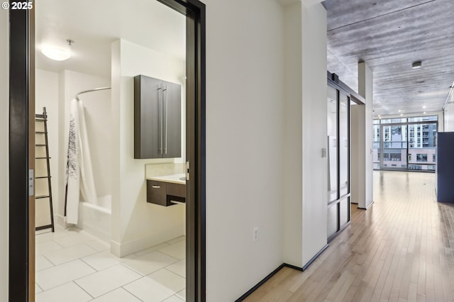 corridor featuring a wall of windows, baseboards, and light wood finished floors