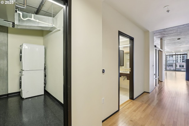 hall with a wall of windows, baseboards, stacked washer and dryer, and wood finished floors