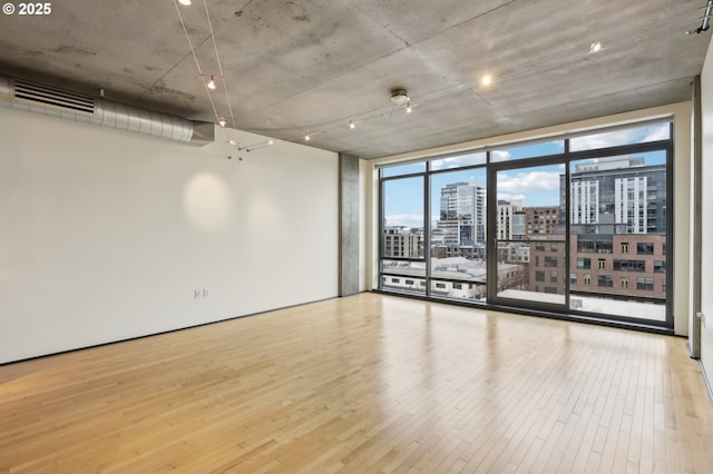 spare room with visible vents, floor to ceiling windows, a view of city, and wood finished floors