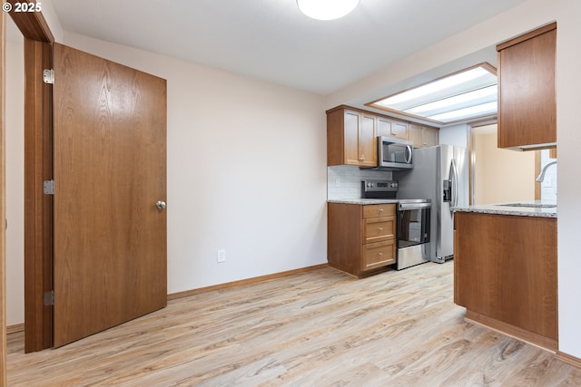 251 NE Village Squire Ave Unit 15, Gresham, OR 97030 - kitchen with stainless steel appliances, light wood-type flooring, a sink, brown cabinetry, and light stone counters