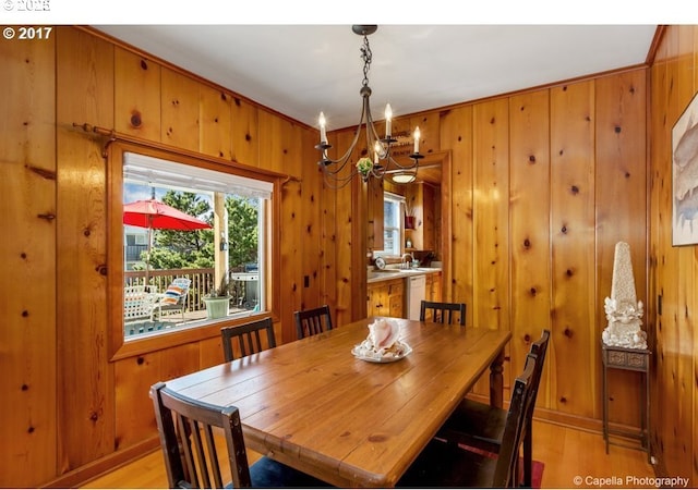 dining room featuring light wood-style floors, wood walls, and a notable chandelier