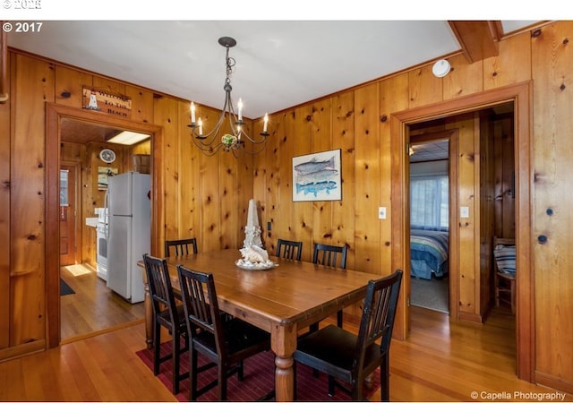 dining space featuring wooden walls, light wood-style floors, and an inviting chandelier