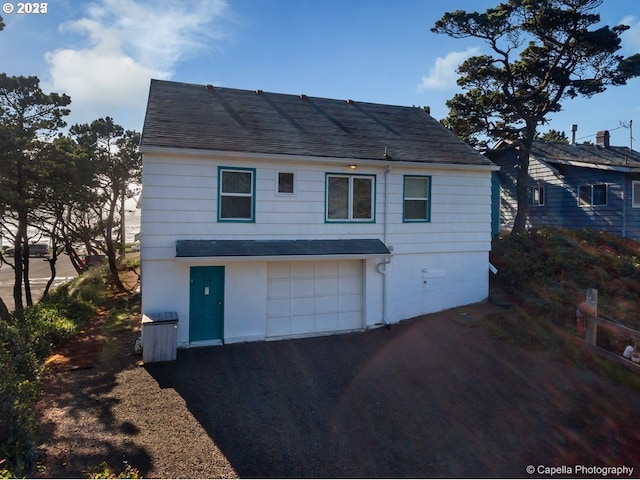 rear view of house featuring a garage, driveway, and a shingled roof