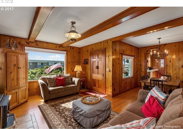living area featuring wood walls, a notable chandelier, beamed ceiling, and light wood-style flooring