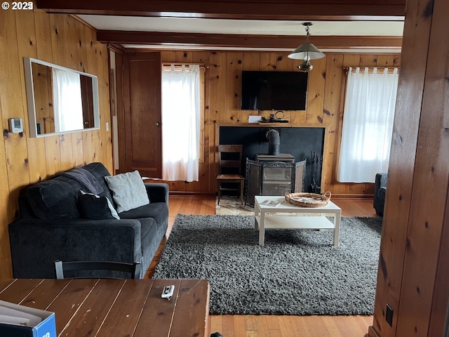 living area with beamed ceiling, a wood stove, wood finished floors, and a healthy amount of sunlight