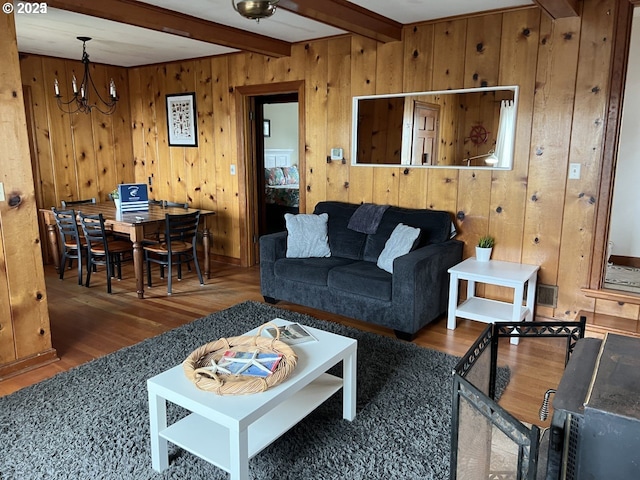 living room with visible vents, wood finished floors, wood walls, a notable chandelier, and beam ceiling