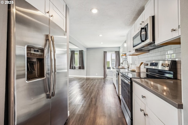 63 S 22nd St, Saint Helens, OR 97051 - kitchen featuring appliances with stainless steel finishes, dark wood-style floors, dark countertops, baseboards, and white cabinetry